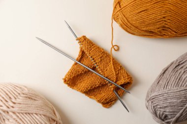 Yumuşak renkli iplikler, örgü örme ve bej arkaplanda metal iğneler, düz bir zemin.