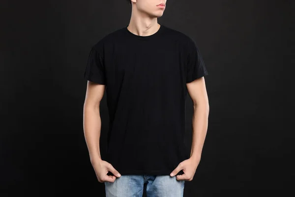 Man wearing stylish t-shirt on black background, closeup. Mockup for design