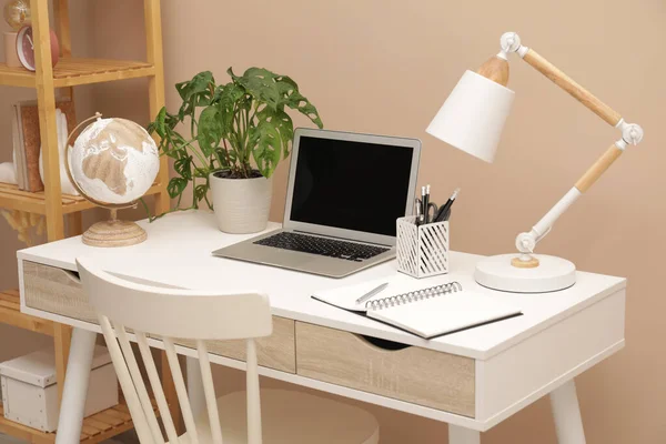 Cozy workplace with modern laptop on desk and comfortable chair at home