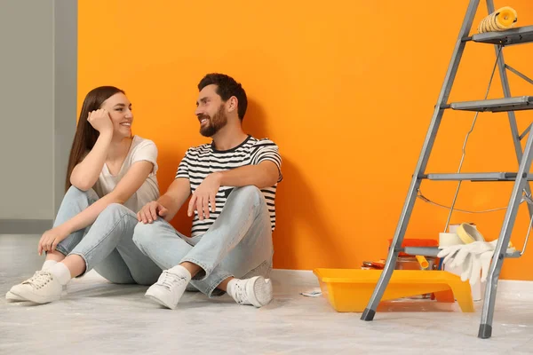 Счастливые Дизайнеры Сидят Полу Покрасочным Оборудованием Рядом Свежевыкрашенными Оранжевыми Стенами — стоковое фото