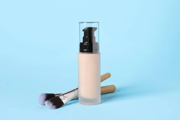 Bottle of skin foundation and brushes on light blue background. Makeup product