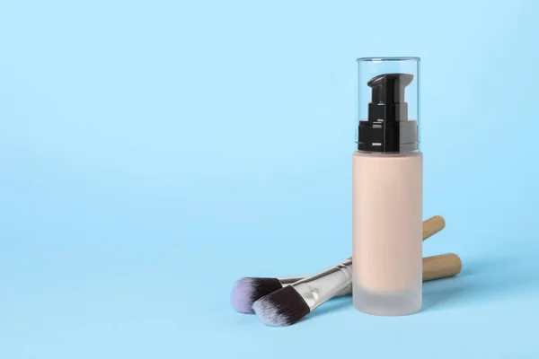 Bottle of skin foundation and brushes on light blue background, space for text. Makeup product