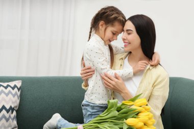 Kızıyla mutlu bir kadın ve evdeki kanepede sarı laleler, mesaj için yer. Anneler günü kutlaması.