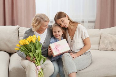 Küçük kız, annesini ve büyükannesini çiçekler ve hediyelerle tebrik ediyor. Anneler Günün kutlu olsun.