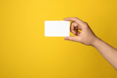 Sarı arka planda boş hediye kartı tutan kadın, yakın plan.