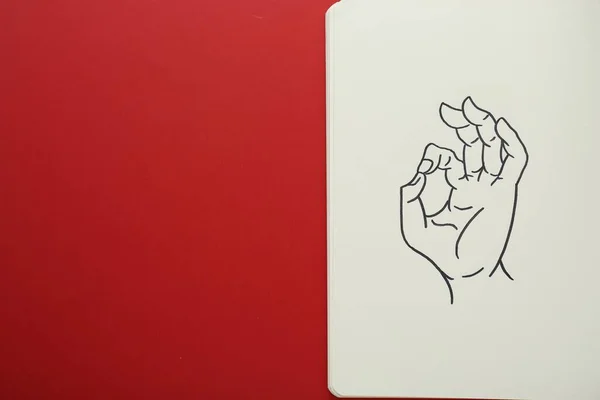 Notebook with drawing of hand showing okay gesture on red background, top view. Space for text