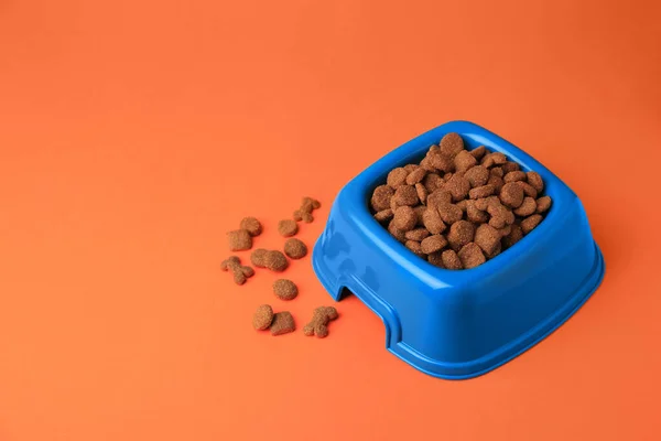 Dry pet food in feeding bowl on orange background. Space for text
