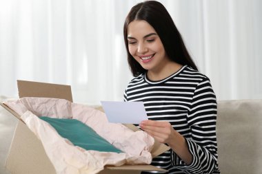 Kutlama kartı taşıyan mutlu bir kadın. Yanında Noel hediyesi olan bir paket.