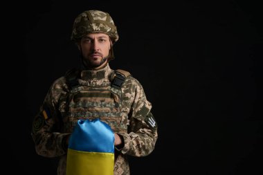 Soldier in military uniform with Ukrainian flag on black background clipart