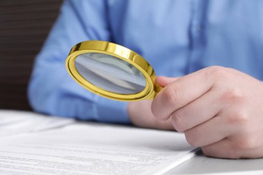 Beyaz masada büyüteçle belgeye bakan adam, yakın plan. Konsept aranıyor