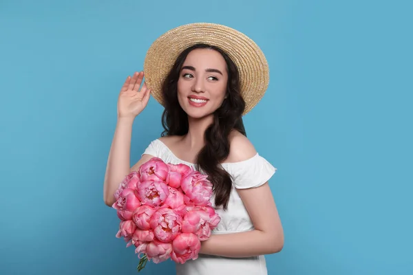 美しいです若いです女性でわら帽子でピンク牡丹の花束とともにライトブルーの背景 — ストック写真