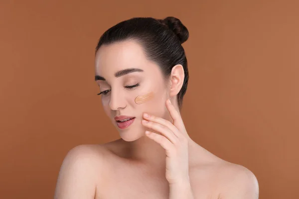 stock image Woman with swatch of foundation on face against brown background