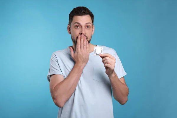 Confused man holding condom on light blue background