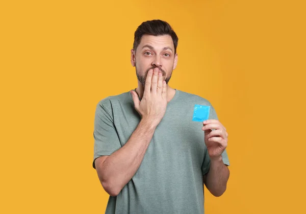 Confused Man Holding Condom Orange Background — Stock Photo, Image