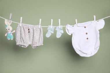 Sevimli küçük bebek kıyafetleri ve oyuncak yeşil arka planda çamaşır ipine asılı.