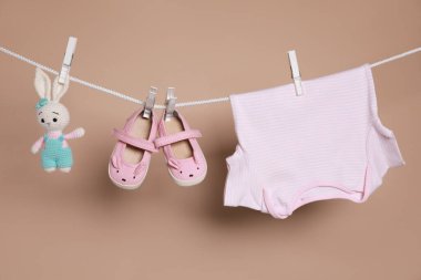 Şirin küçük bebek ayakkabıları, tişört ve oyuncak kahverengi arka planda çamaşır ipine asılı.