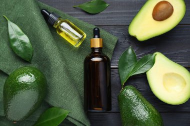 Temel yağlı şişeler, olgun taze avokadolar ve siyah ahşap masa üzerinde yapraklar, düz yatıyordu.