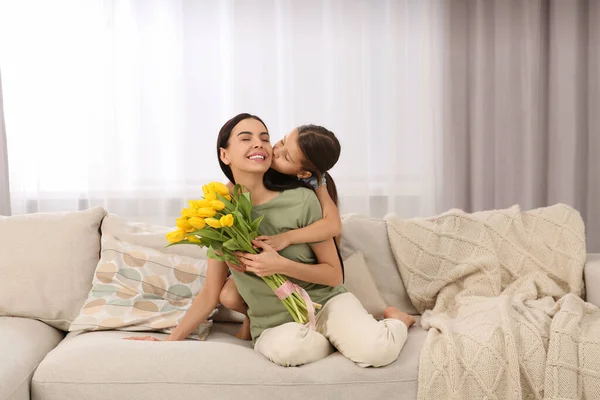 快乐的女人和她可爱的女儿在家里的沙发上放着一束黄色郁金香 母亲节庆祝活动 — 图库照片