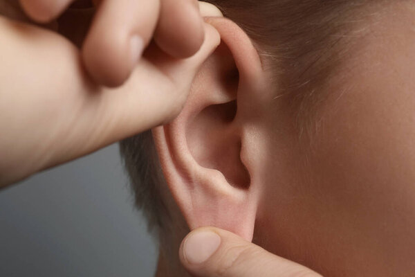 Boy touching his ear on grey background, closeup