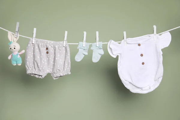かわいい小さな赤ちゃんの服やおもちゃは緑の背景に洗濯ラインにぶら下がっている — ストック写真