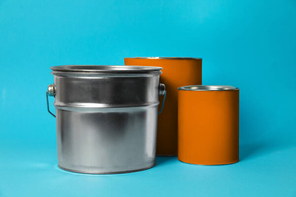 Cans and bucket of orange paint on turquoise background