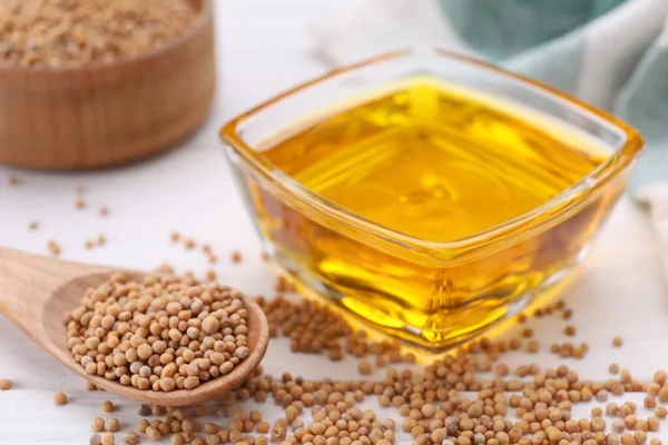 stock image Bowl of natural oil and mustard seeds on white table, closeup