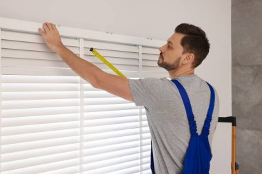 İçeriye yatay pencereler kurarken mezura kullanan üniformalı işçiler