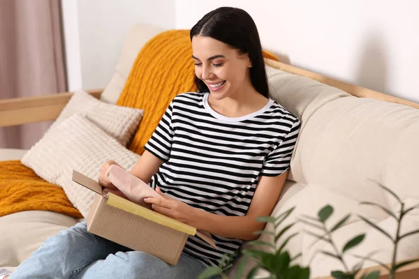 快乐的年轻女人在家里的沙发上打开包裹 网上购物 — 图库照片