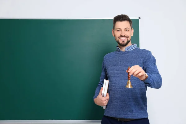 Teacher with school bell near chalkboard indoors. Space for text