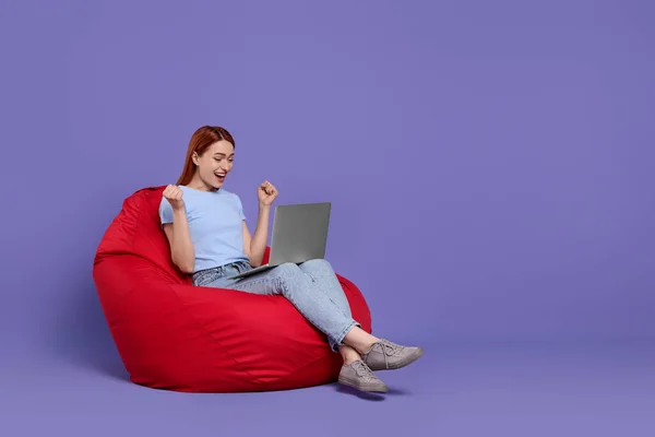 Jovem Feliz Com Laptop Sentado Cadeira Beanbag Contra Fundo Lilás — Fotografia de Stock