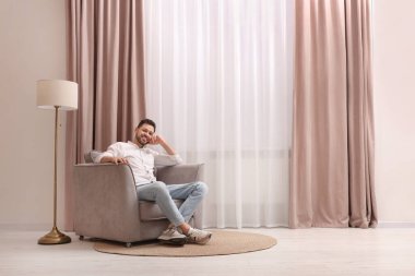 Evdeki güzel perdelerle pencerenin yanındaki koltukta dinlenen mutlu adam. Metin için boşluk
