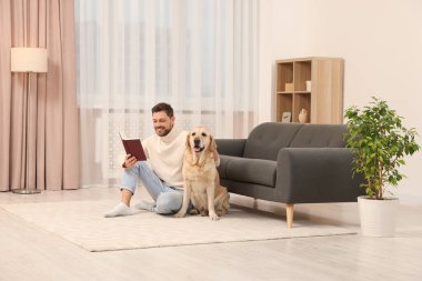 Adam yerde kitap okuyor. Evindeki şirin Labrador Retriever 'ının yanında.