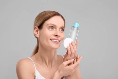 Makyaj temizleyicisi ve gri arka planda pamuk pedi olan güzel bir kadın.