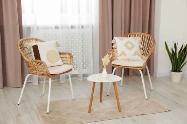 Pastel pencere perdeleri, ahşap masa ve rattan sandalyeli oturma odası.