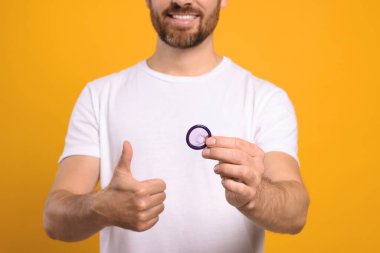 Prezervatifli bir adam sarı arka planda baş parmağını gösteriyor, yakın plan. Güvenli seks.