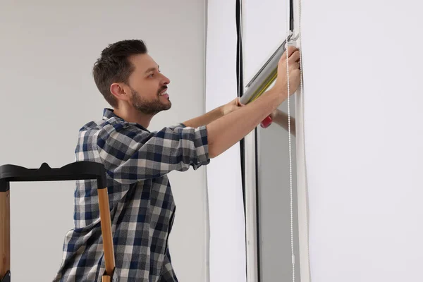Man measuring window with tape on stepladder indoors. Roller blinds installation