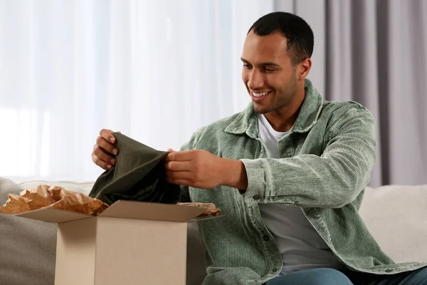 Happy young man opening parcel at home. Internet shopping