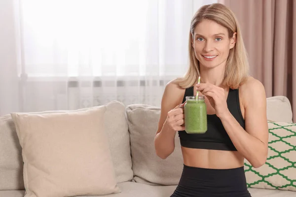 stock image Young woman in sportswear with mason jar of fresh smoothie at home, space for text