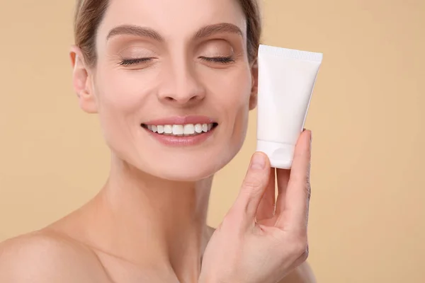 stock image Woman holding tube of foundation on beige background