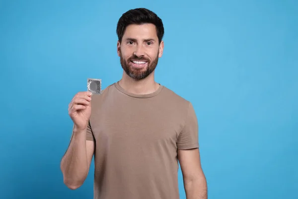 Szczęśliwy Człowiek Trzymający Prezerwatywę Jasnoniebieskim Tle Miejsce Tekst Bezpieczny Seks — Zdjęcie stockowe