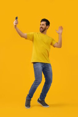 Mutlu adam sarı arka planda akıllı telefonlu selfie çekiyor, mesaj için yer var.