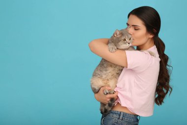 Genç bir kadın açık mavi arka planda sevimli kedisini öpüyor, mesaj için yer var.