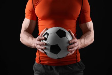 Siyah arka planda futbol topu olan atletik adam, yakın plan.
