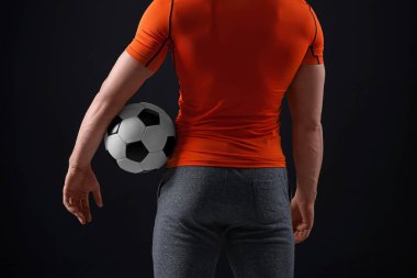 Siyah arka planda futbol topu olan atletik adam, yakın plan.