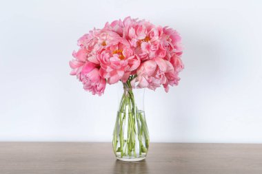 Güzel bir buket pembe şakayık vazoda, ahşap masada beyaz arka planda.