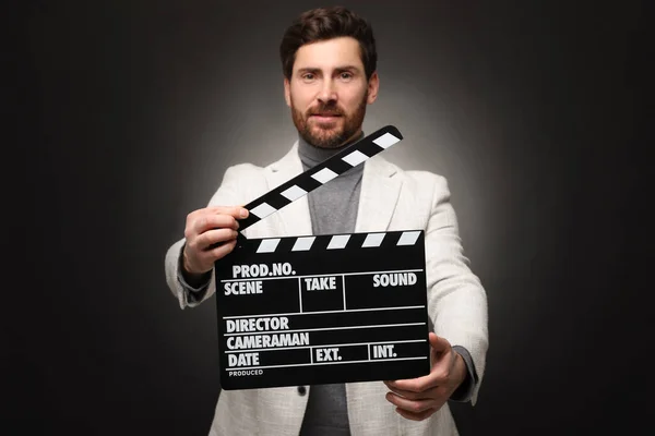 Adult actor holding clapperboard on black background