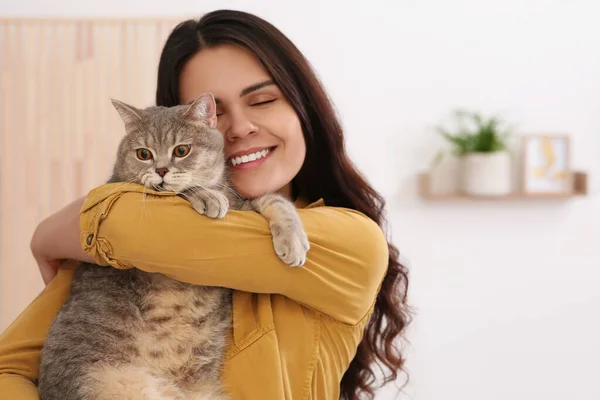 Young woman with adorable cat at home, space for text
