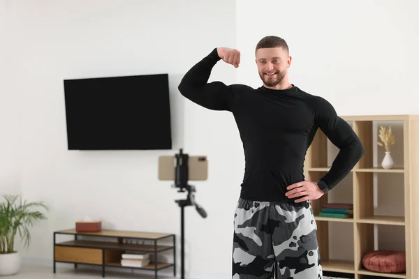 训练者在家里用电话在网上上健身课的时候展示他的肌肉 — 图库照片