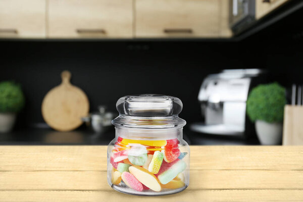 Glass jar with tasty gummy candies on wooden table in kitchen