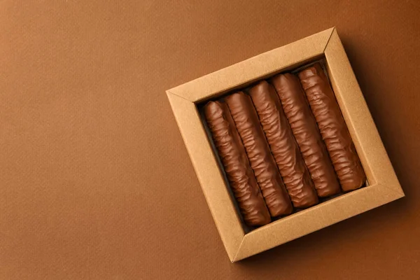 Sweet tasty chocolate bars in box on brown background, top view. Space for text